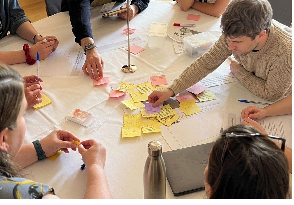 Live collaboration session — multi-disciplinary team working through sticky notes around a table